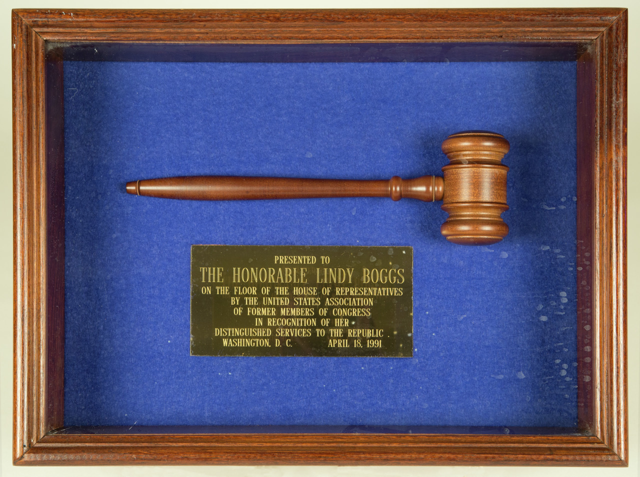 A wooden gavel mounted in a display box with a blue background. Below it is a plaque dedicated to The Honorable Lindy Boggs, recognizing distinguished services to the Republic, dated April 18, 1991.