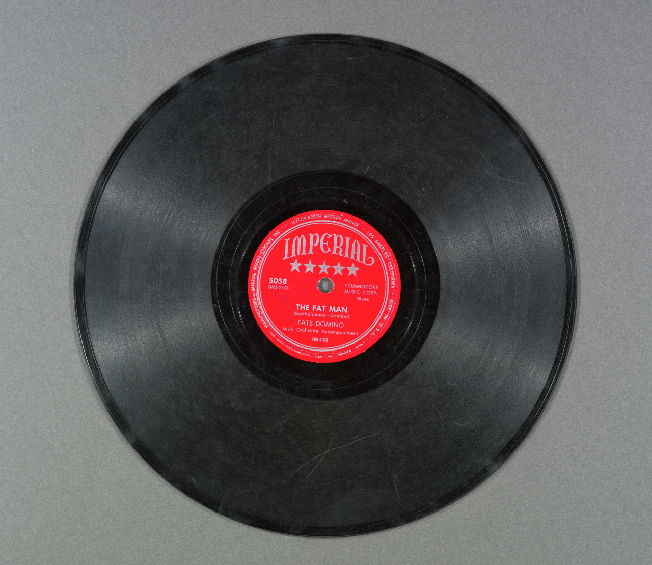 A vintage vinyl record with a red label in the center, titled The Fat Man by Fats Domino, from Imperial Records. The background is a textured gray surface.