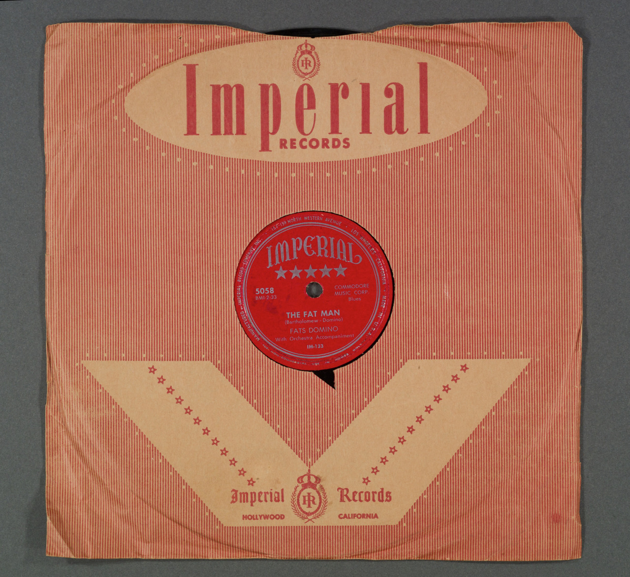 A vintage 78 RPM record with a red label in a brown paper sleeve. The label reads The Fat Man by Fats Domino and Imperial Records is printed at the top in red letters. The sleeve features a decorative design and Hollywood, California address.