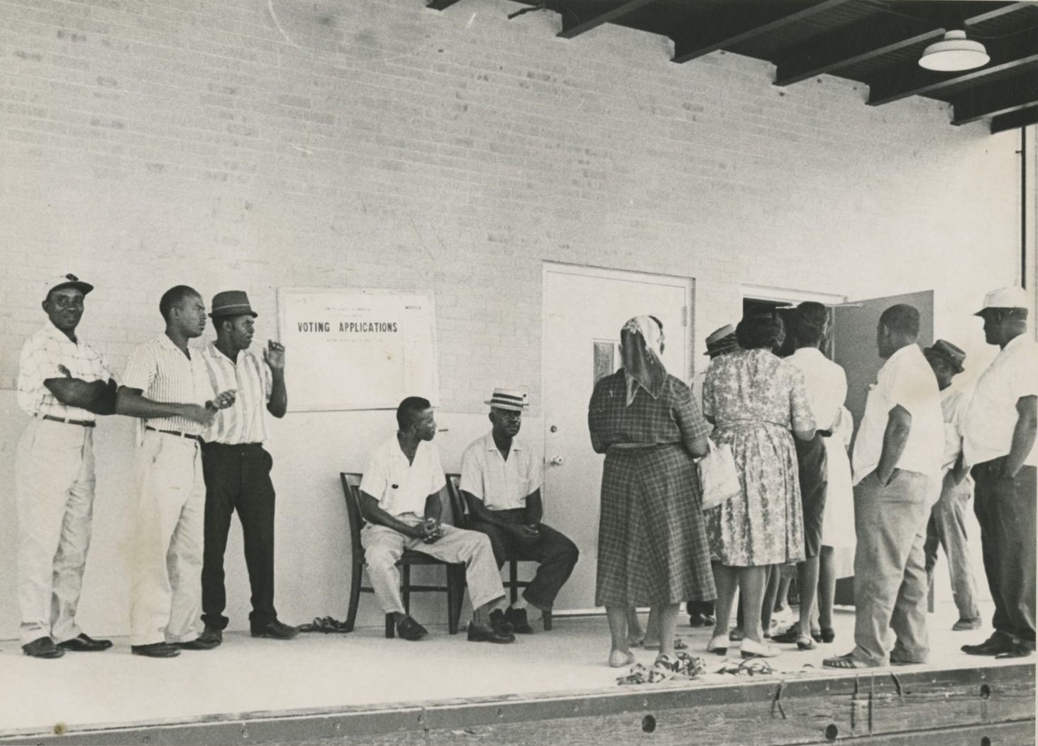 A press photograph featuring about a dozen Black men and women in a voter registration line outside the post office in Buras, Louisiana.
