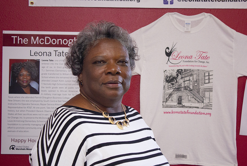 A woman wearing a striped shirt stands in front of a wall with a display about the Leona Tate Foundation for Change. The display includes a t-shirt and a poster with information about an honoree named Leona Tate.