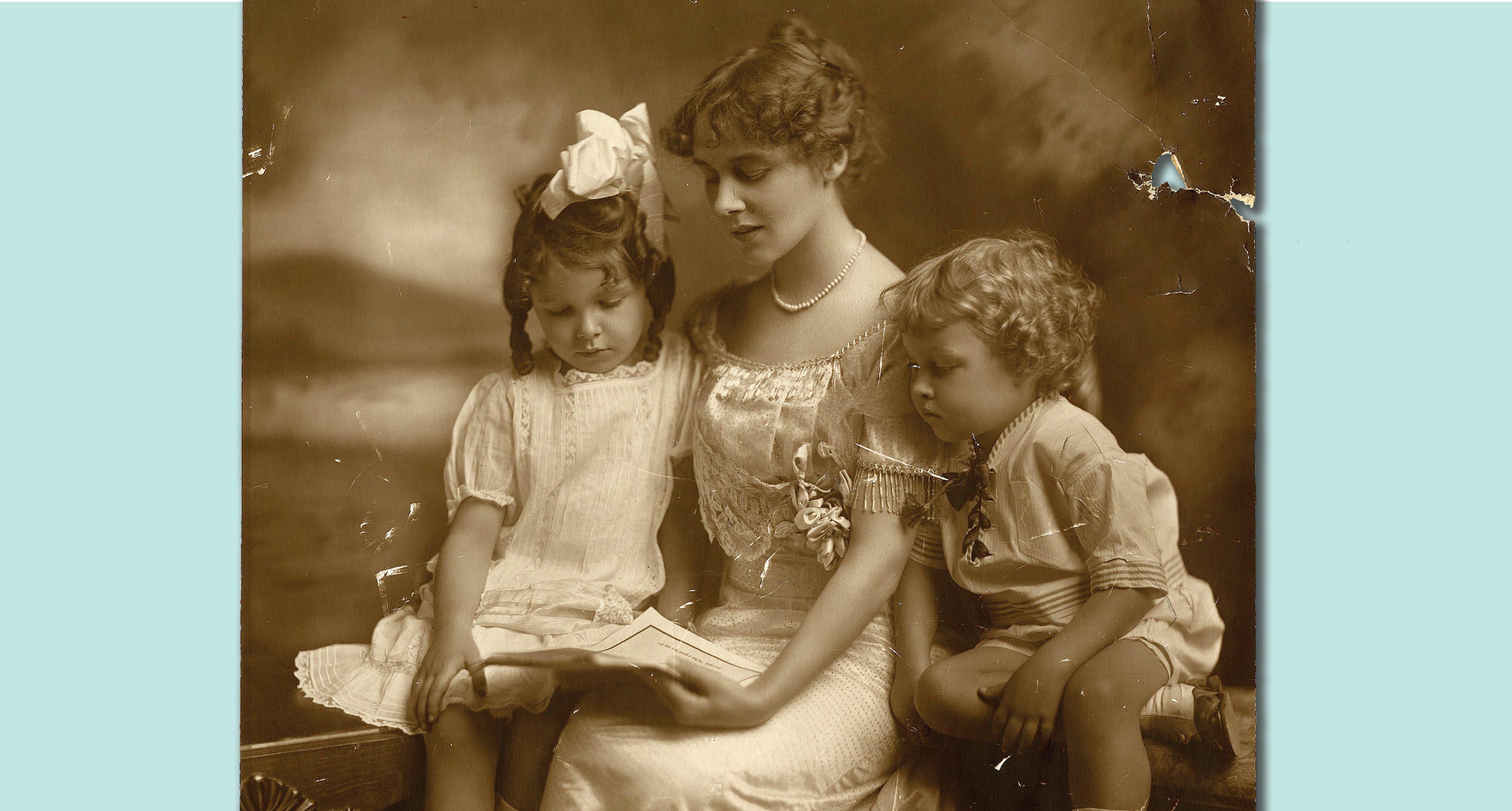 A vintage sepia photograph shows a young woman reading to two children. The woman, wearing a white dress, appears focused on the book. The children, a girl on her left and a boy on her right, listen attentively. The background is softly blurred.