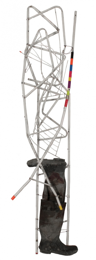 An abstract sculpture featuring a twisted metal structure with various colored accents atop a single rubber boot base. The sculpture has a tall, slender form with geometric shapes.