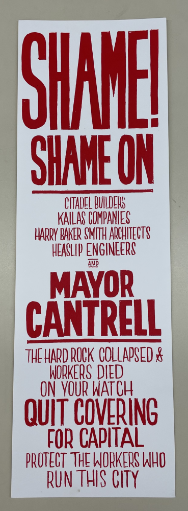 Protest sign in bold red text on white background. It criticizes Citadel Builders, Kailas Companies, Harry Baker Smith Architects, Heaslip Engineers, and Mayor Cantrell for a building collapse and urges protection of workers over capital interests.