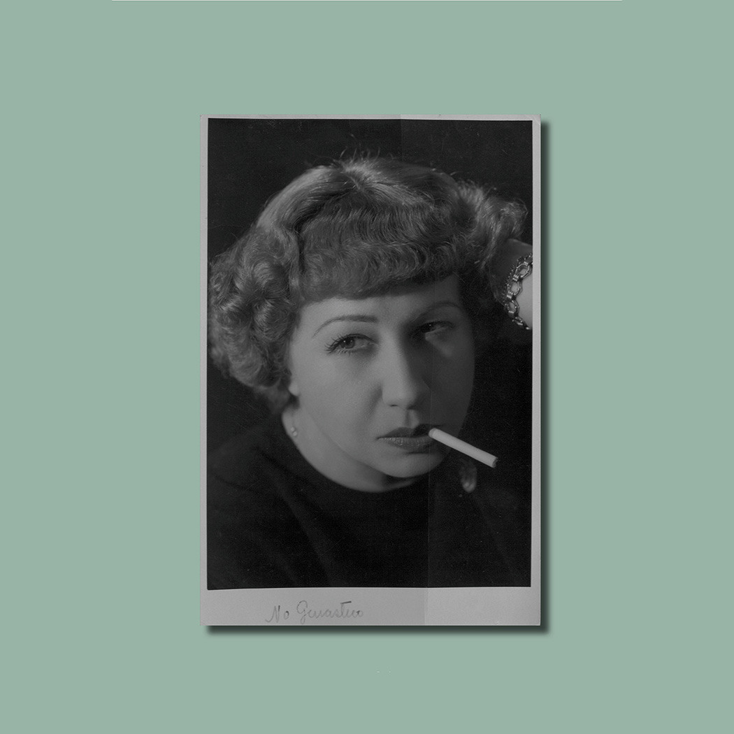 Black and white portrait of a person with short, curly hair, holding a cigarette. The image is set against a solid light green background. Theres a handwritten signature below the photograph.