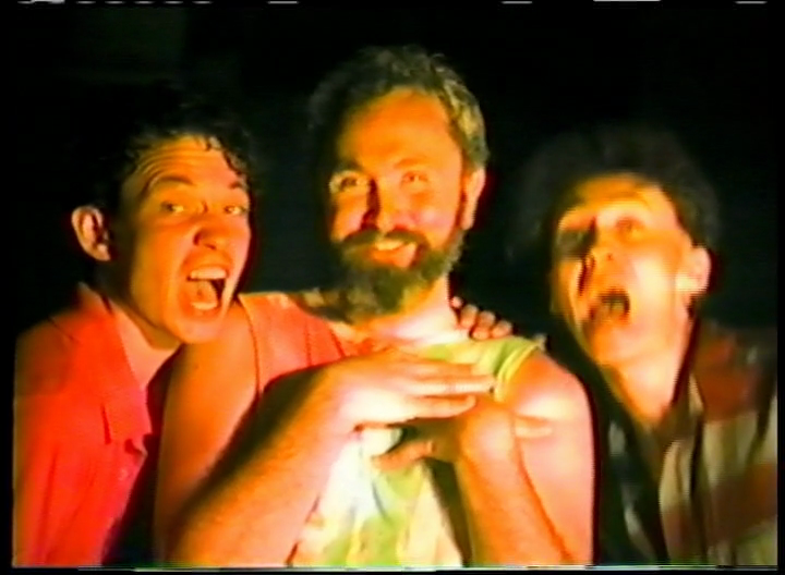 Three people pose with exaggerated expressions. The person in the center has a beard and is smiling with hands together. The two people on either side are looking at the camera with wide mouths and animated expressions. The lighting is warm.