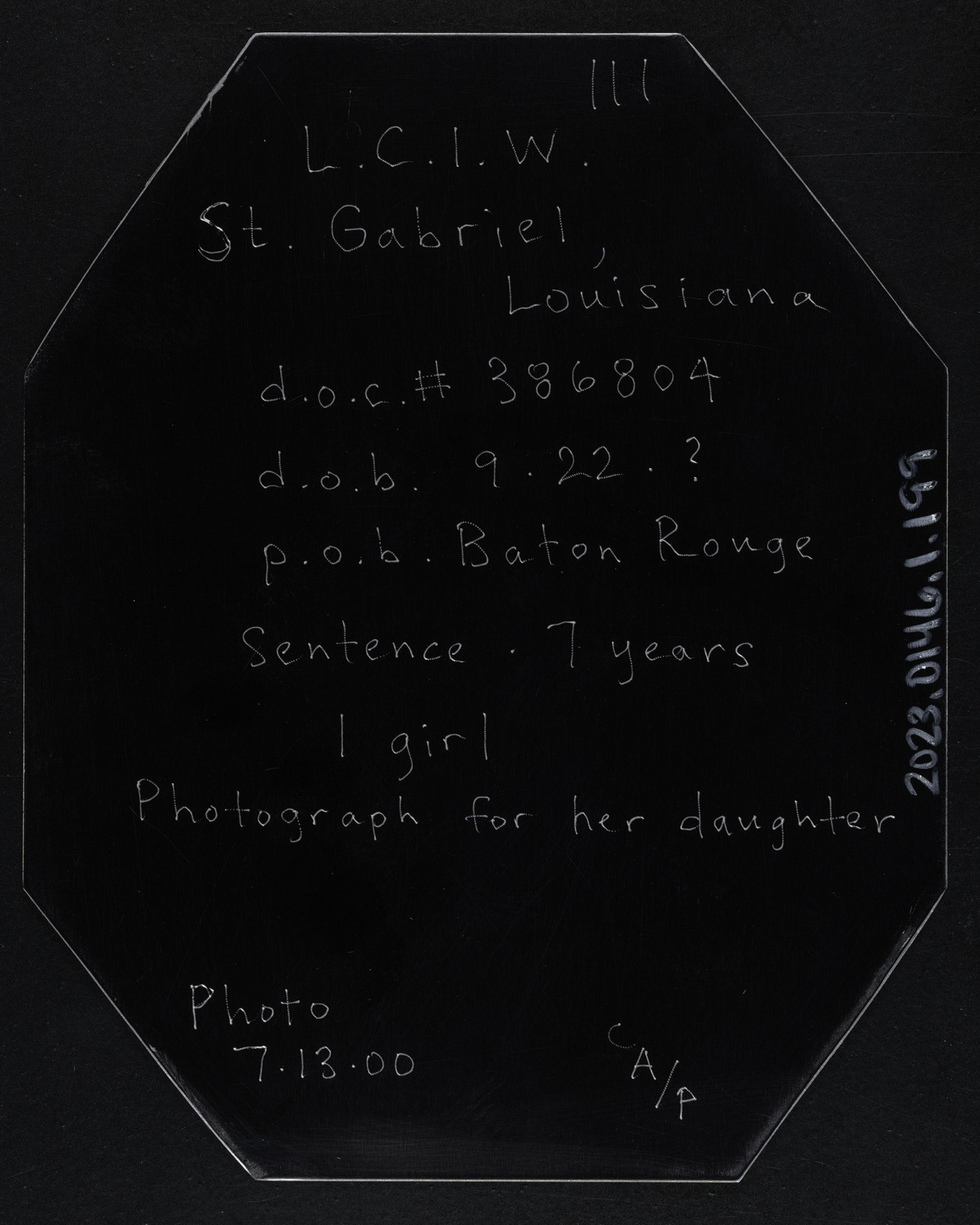 A view of the reverse side of a tintype-style photograph of a prison inmate, printed on metal, which has text describing information about the portrait subject.