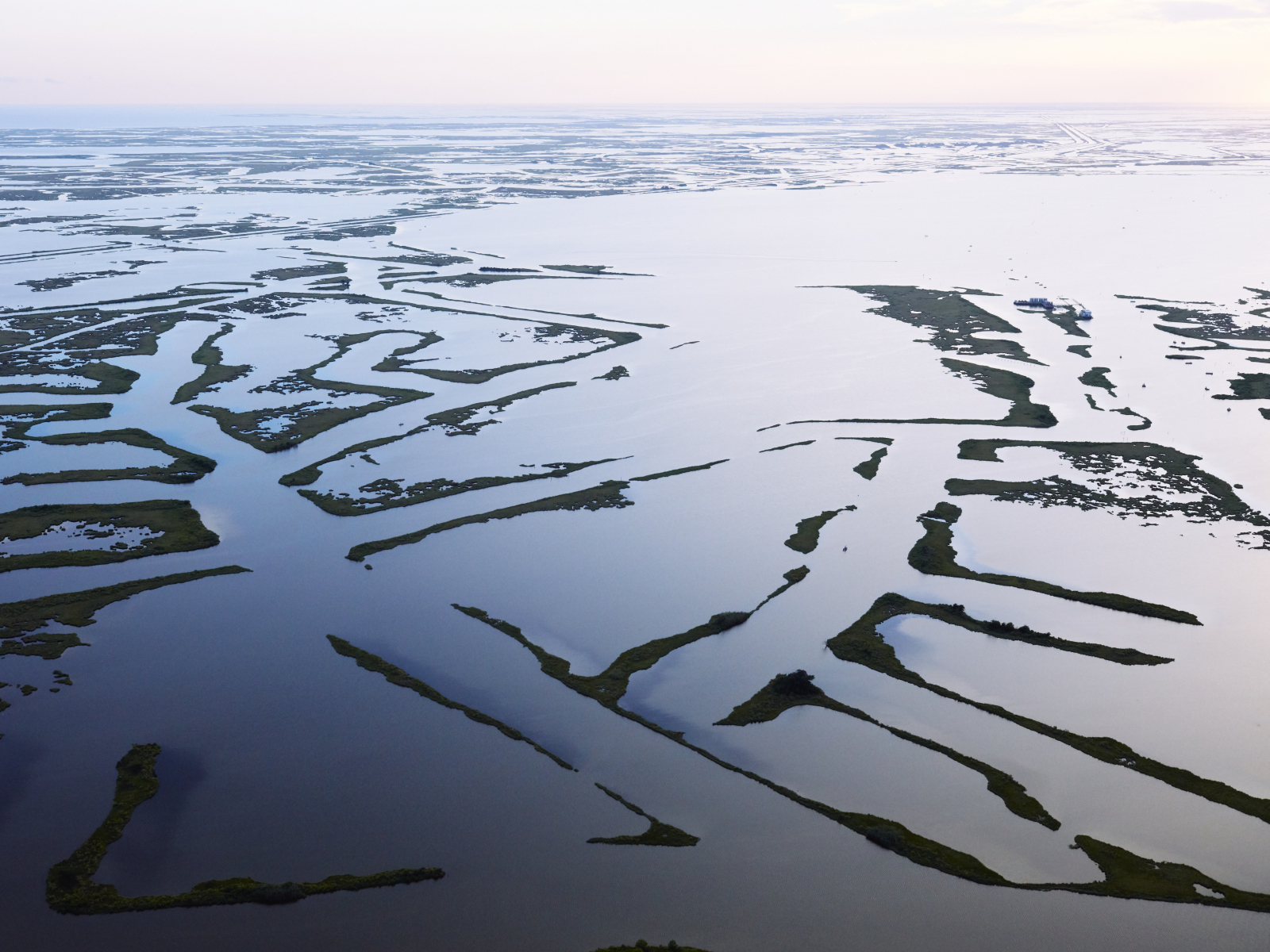 An aerial photo shows navigation channels near Golden Meadow leave a spiderweb of remaining marshland, with open water dominating the landscape into the distant horizon.