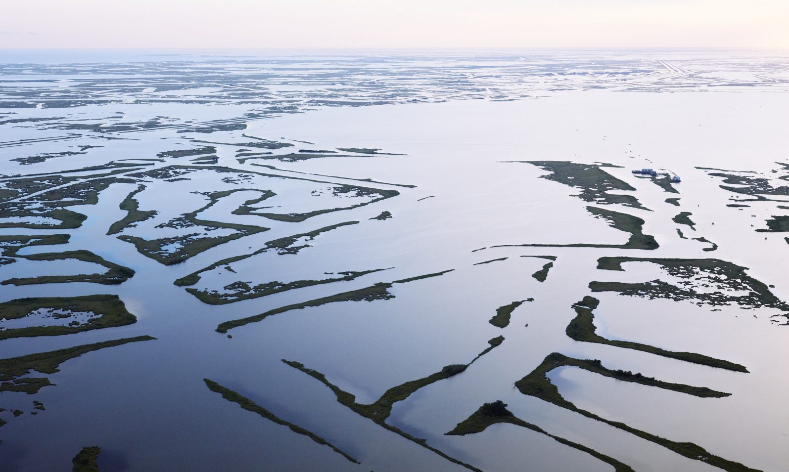 An aerial photo shows navigation channels near Golden Meadow leave a spiderweb of remaining marshland, with open water dominating the landscape into the distant horizon.