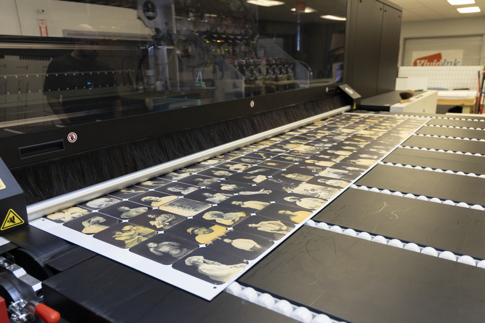 A photo shows a collage of portrait prints coming off of a large professional printing press.