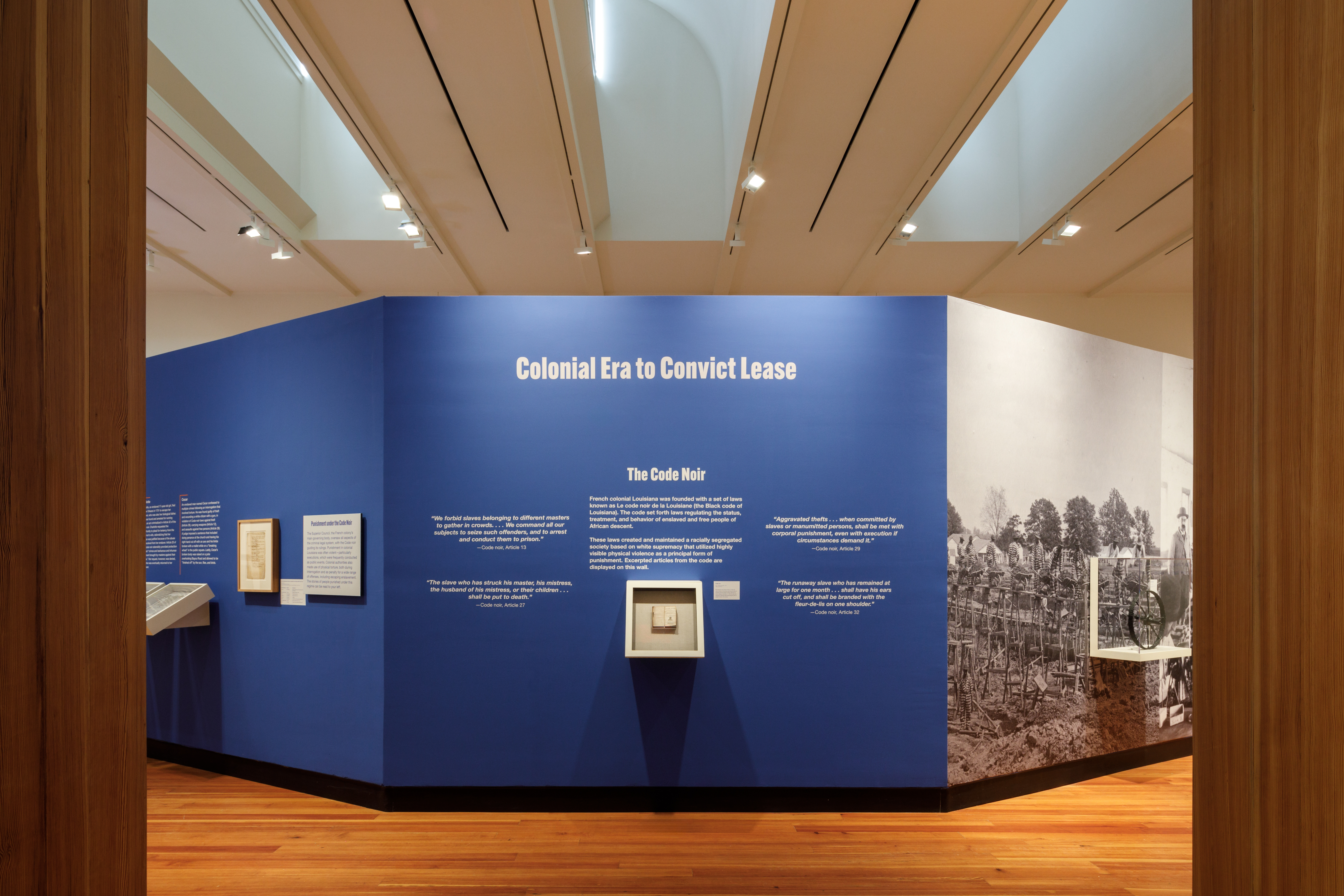 Museum exhibit titled Colonial Era to Convict Lease featuring blue walls with text, historical documents, and photographs. The display provides an educational overview of historical penal systems and associated codes.