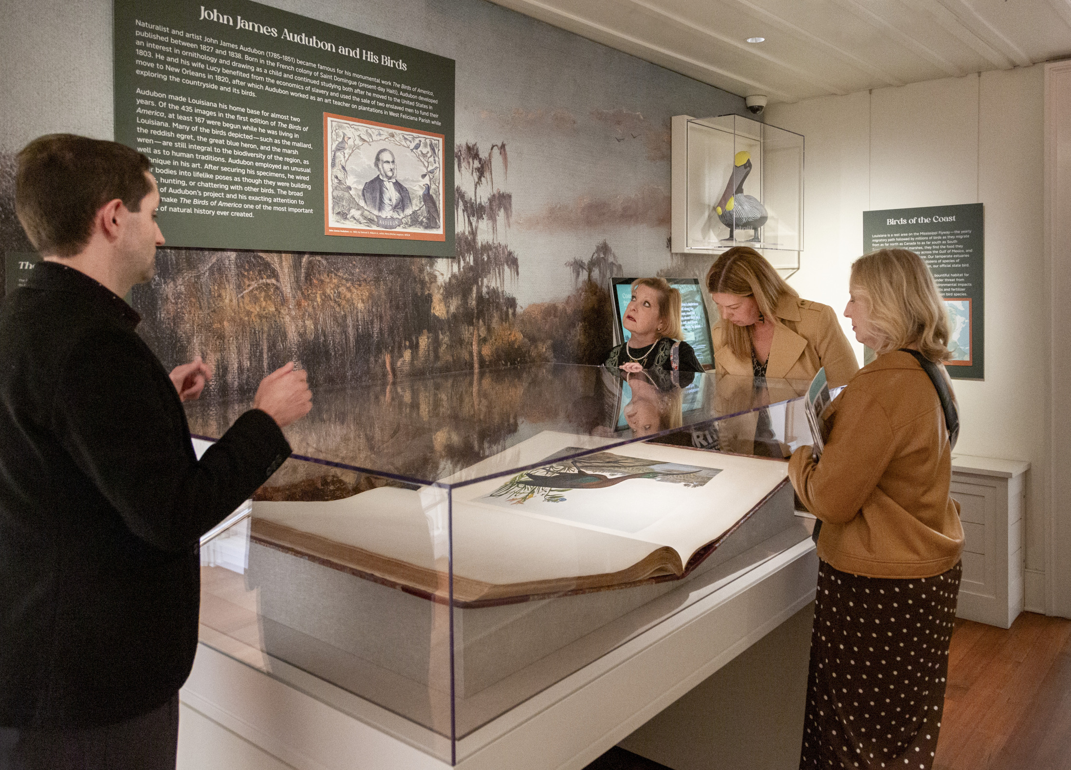 A group of people examine the Audubon Folio, a large book of artworks depicting birds, on view at the "A Vanishing Bounty" exhibition at HNOC.