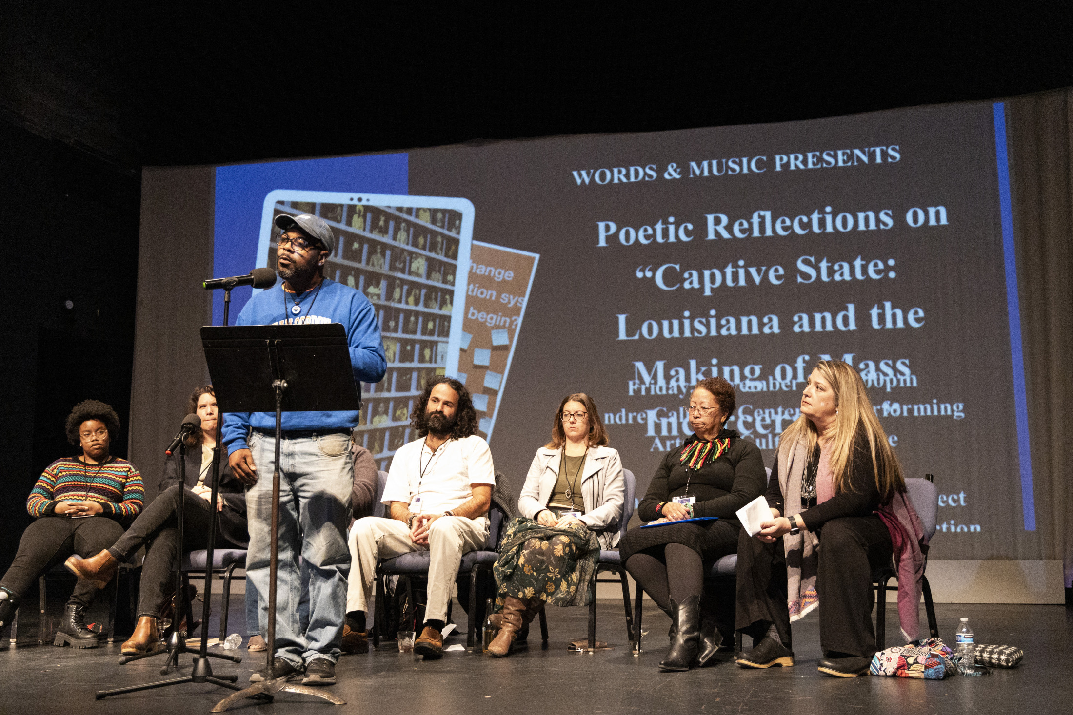 A diverse group of people on stage for a panel discussion titled “Poetic Reflections on ‘Captive State: Louisiana and the Making of Mass Incarceration.’” One speaker stands at a podium while others are seated.