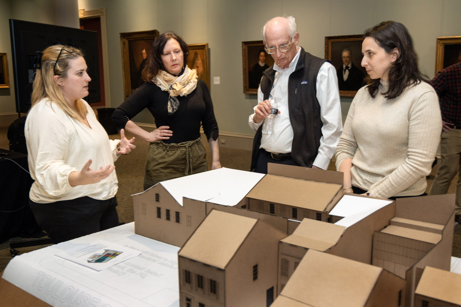 A group of people gather around and discuss a large model mockup, displayed on a table at HNOC.