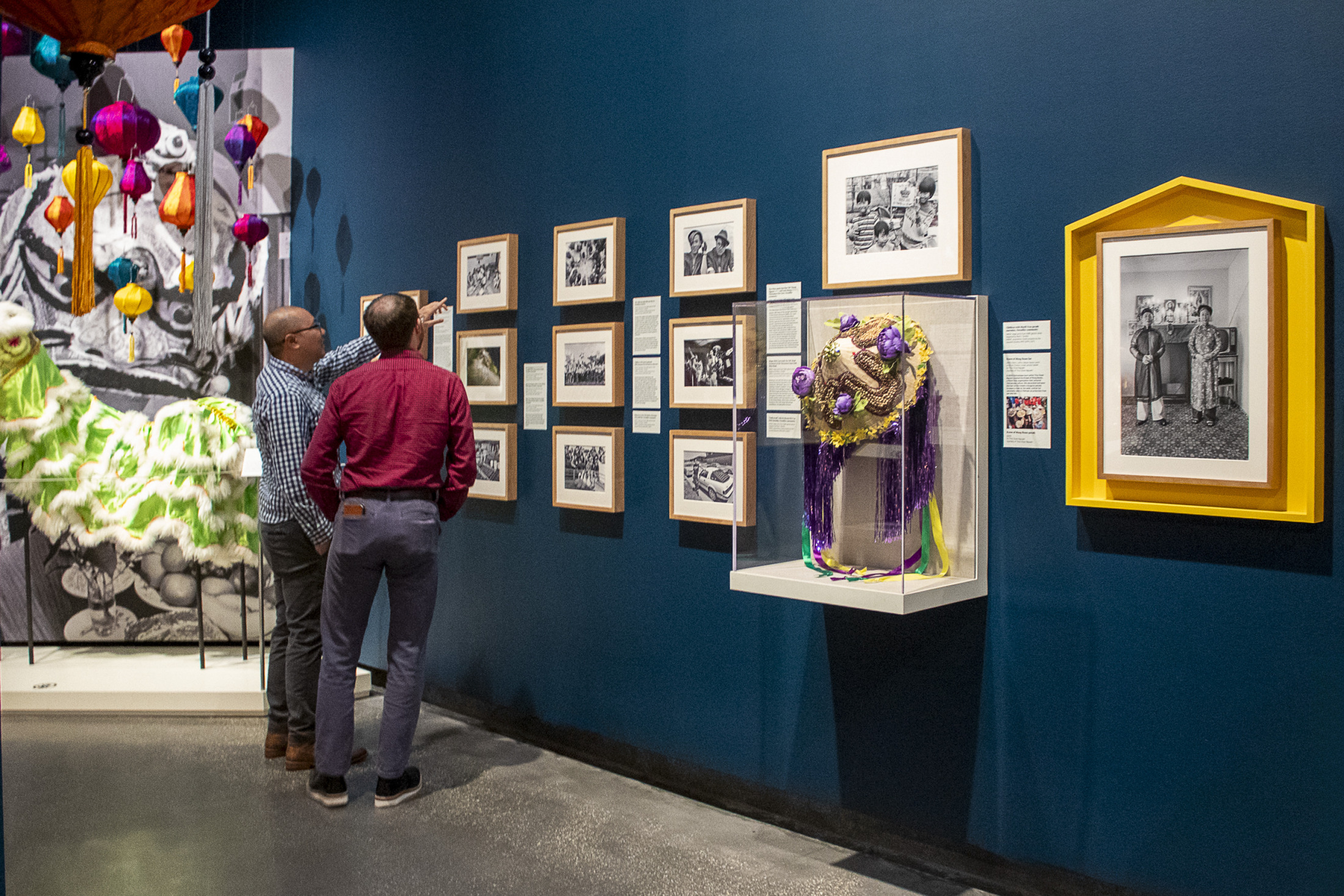 Two men point at photos featured in the HNOC exhibition "Making It Home: From Vietnam to New Orleans."