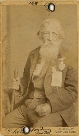 Sepia-toned vintage photo of an elderly man with a long white beard, seated, holding a cane. He wears a suit and has a stern expression. Handwriting and address at the bottom read 151 Canal St., New Orleans.