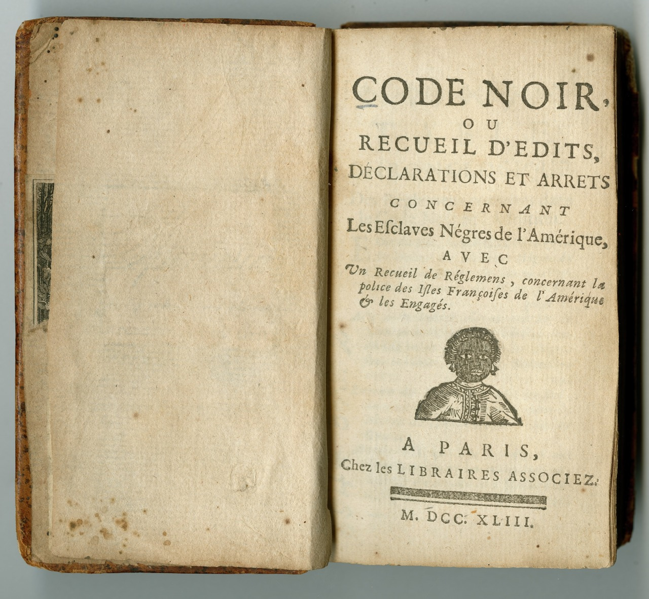 Open book showing the title page of Code Noir, a collection of edicts and declarations concerning enslaved people in America. There is printed text and an illustration of a crowned emblem on the page. Published in Paris, 1743.