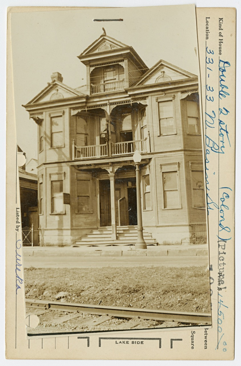 A black-and-white photo of a two-story Victorian house with ornate detailing, featuring a porch and balcony. An inscription on the photo provides the location as 333-335 Boulevard. A streetlamp stands in front of the house.