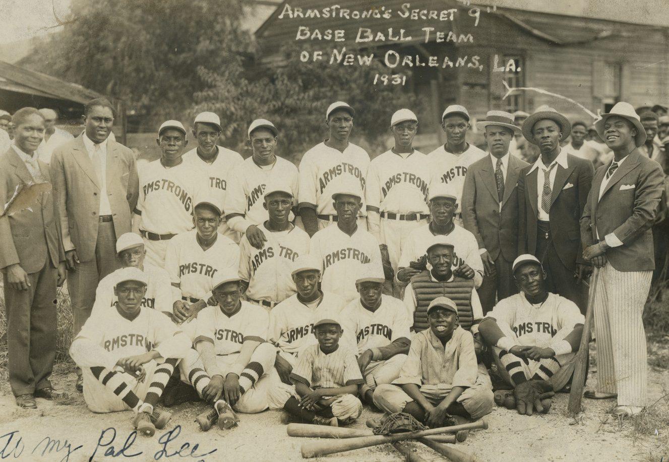 Black and white photo of a baseball team from 1931, New Orleans. The players wear uniforms with Armstrong on them. They are posed with equipment on the ground and are surrounded by suited men. Handwritten note reads To my pal Lee.