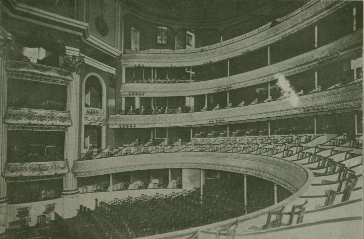 Black and white photo of an empty theater interior with multiple tiers of balconies and ornate design details. Grand architectural features include curved rows of seats and decorative moldings.