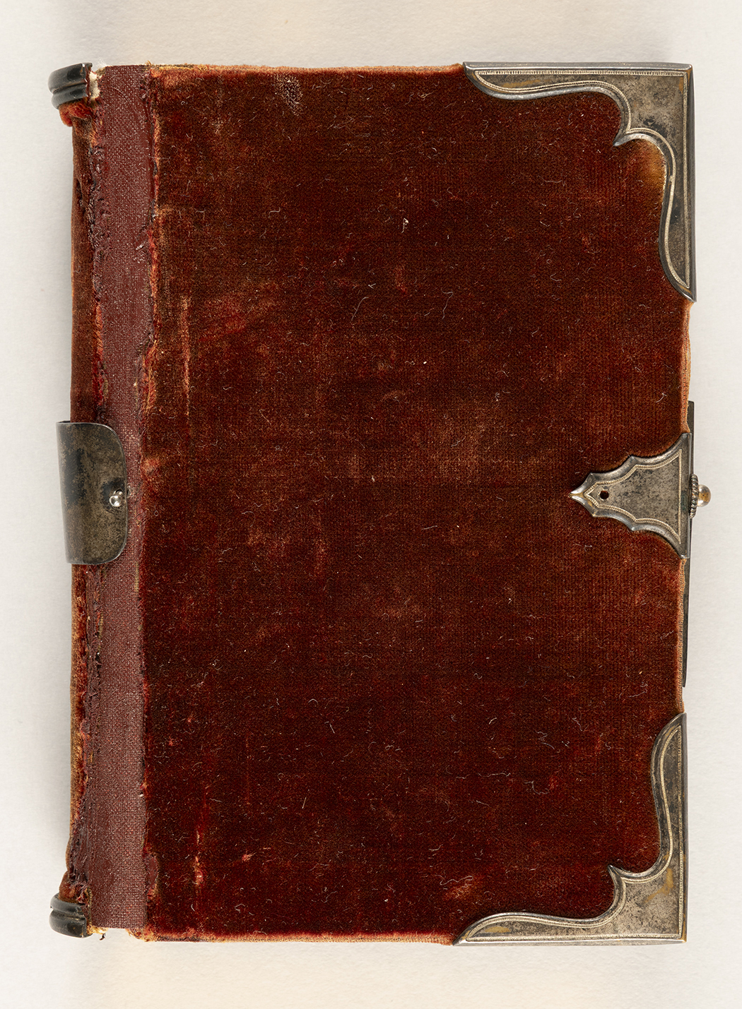 The outside cover of a red velvet-bound prayer book, with decorative corners and clasp made from metal.