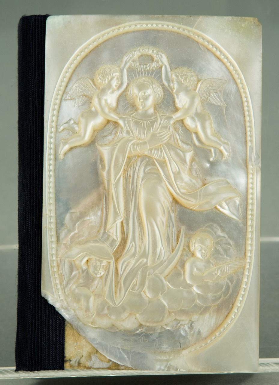 An intricately carved mother-of-pearl panel depicting a female figure surrounded by cherubs, with two angels placing a crown on her head. The artwork features delicate details and raised textures. The panel is set against a black background.