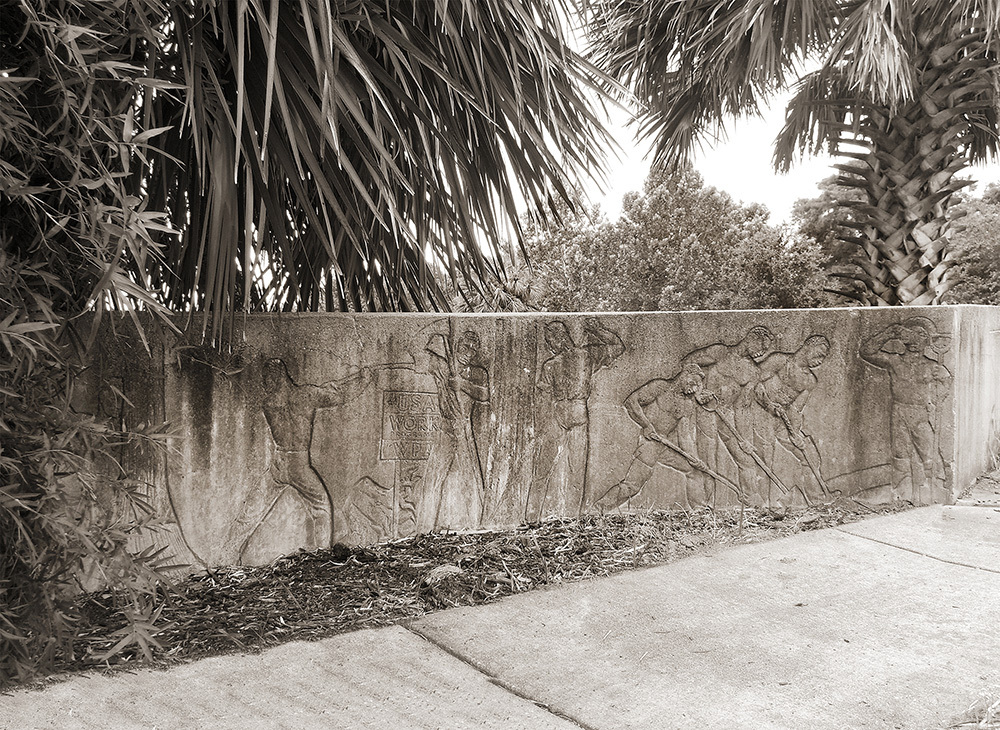 Sepia-toned image of a concrete wall relief depicting figures engaged in various athletic poses, surrounded by palm trees. The artwork features historical athletes in dynamic action, with detailed carvings and lush foliage.