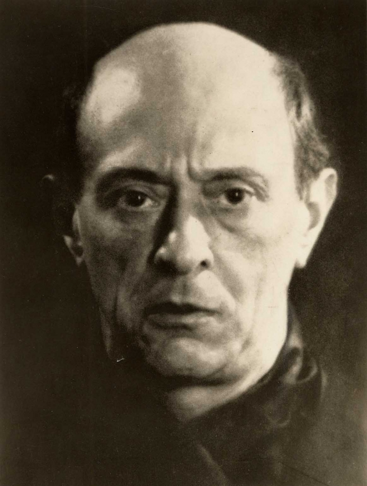 A sepia-toned portrait of a man with a serious expression, looking directly at the camera. He has a receding hairline and wears a dark jacket or robe. The background is dark, highlighting his face.