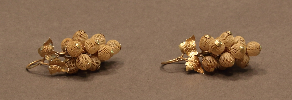 Two intricately designed earrings resembling clusters of grapes, crafted from gold mesh balls with small leaves. They are placed on a plain gray background.