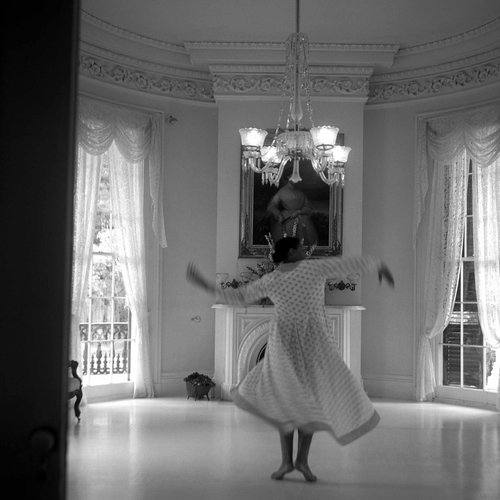 A black and white photo shows artist Carrie Mae Weems dancing inside Nottoway Mansion.