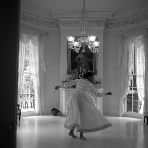 A black and white photo shows artist Carrie Mae Weems dancing inside Nottoway Mansion.
