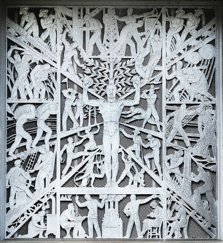 An intricate metal relief sculpture depicting numerous human figures engaged in various activities, such as climbing, lifting, and reaching. At the center, a prominent figure with arms raised stands surrounded by dynamic lines and patterns.