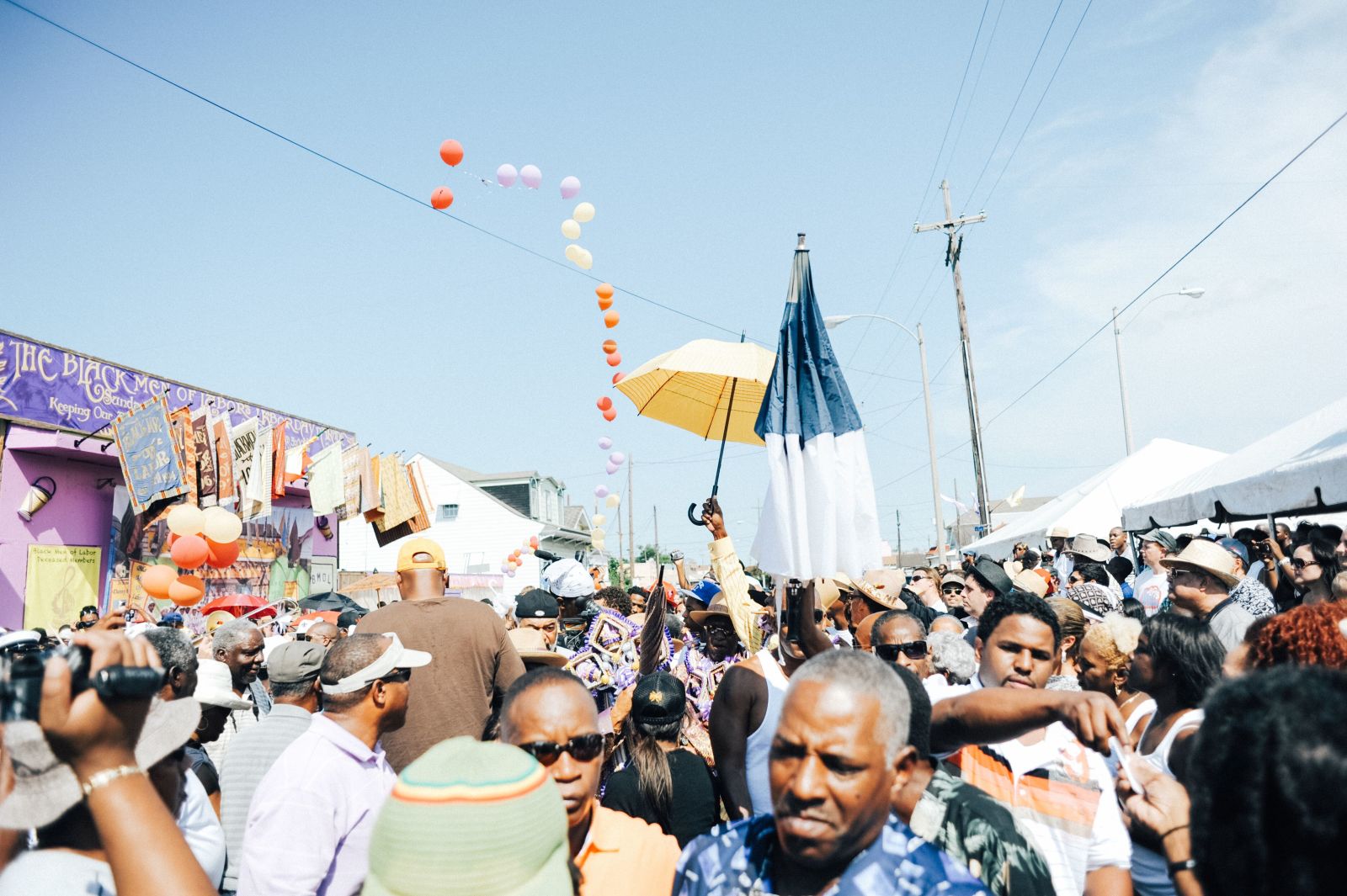 A crowd of participants and onlookers at a Black Men of Labor parade. Colored parasols can be seen being raised among members of the procession.