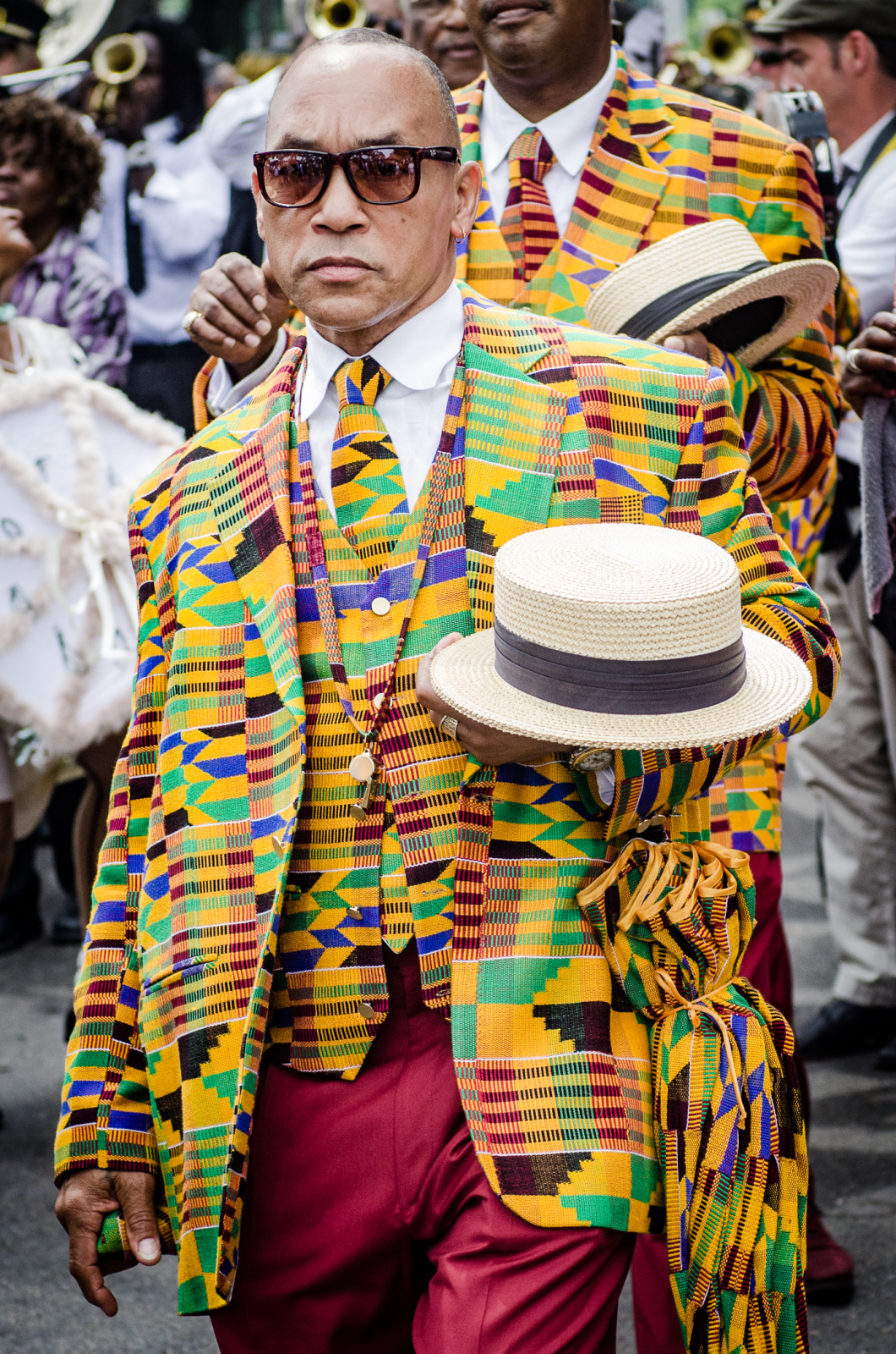 Black Men of Labor club member Fred Johnson, Jr. poses while wearing a vibrantly patterned suit, vest, and tie and sunglasses and holding a white bowler hat in his left land.