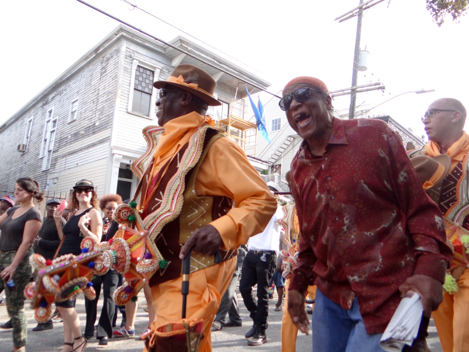 Benny Jones walks with Jerome Smith at a Black Men of Labor parade. Benny is wearing an orange and brown costume, while Jerome is wearing a red patterned shirt and jeans.