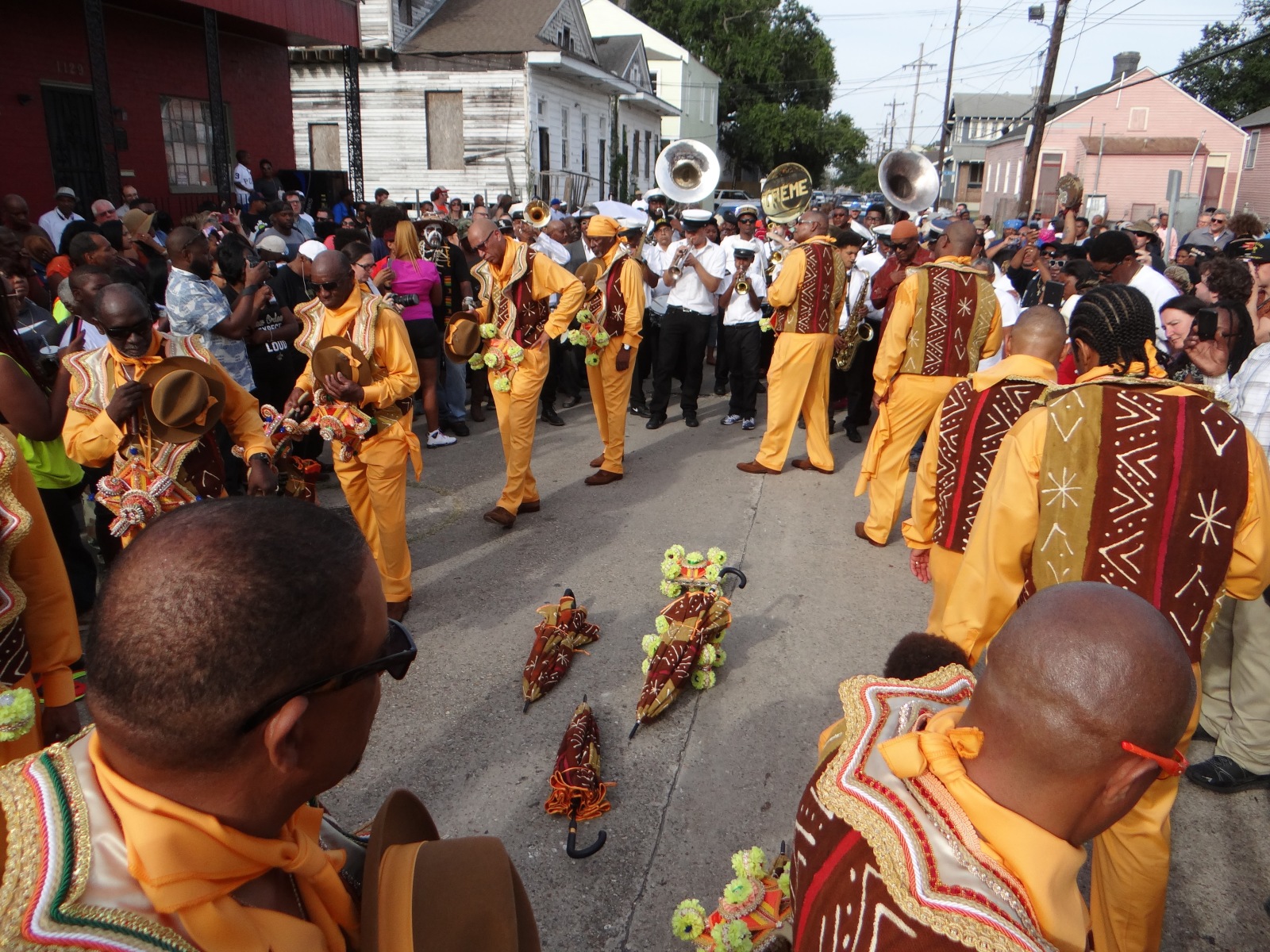 Men of Labor members process around a circle as part of a funeral dirge, in honor of Mark Cerf. They wear orange and red patterned regalia.
