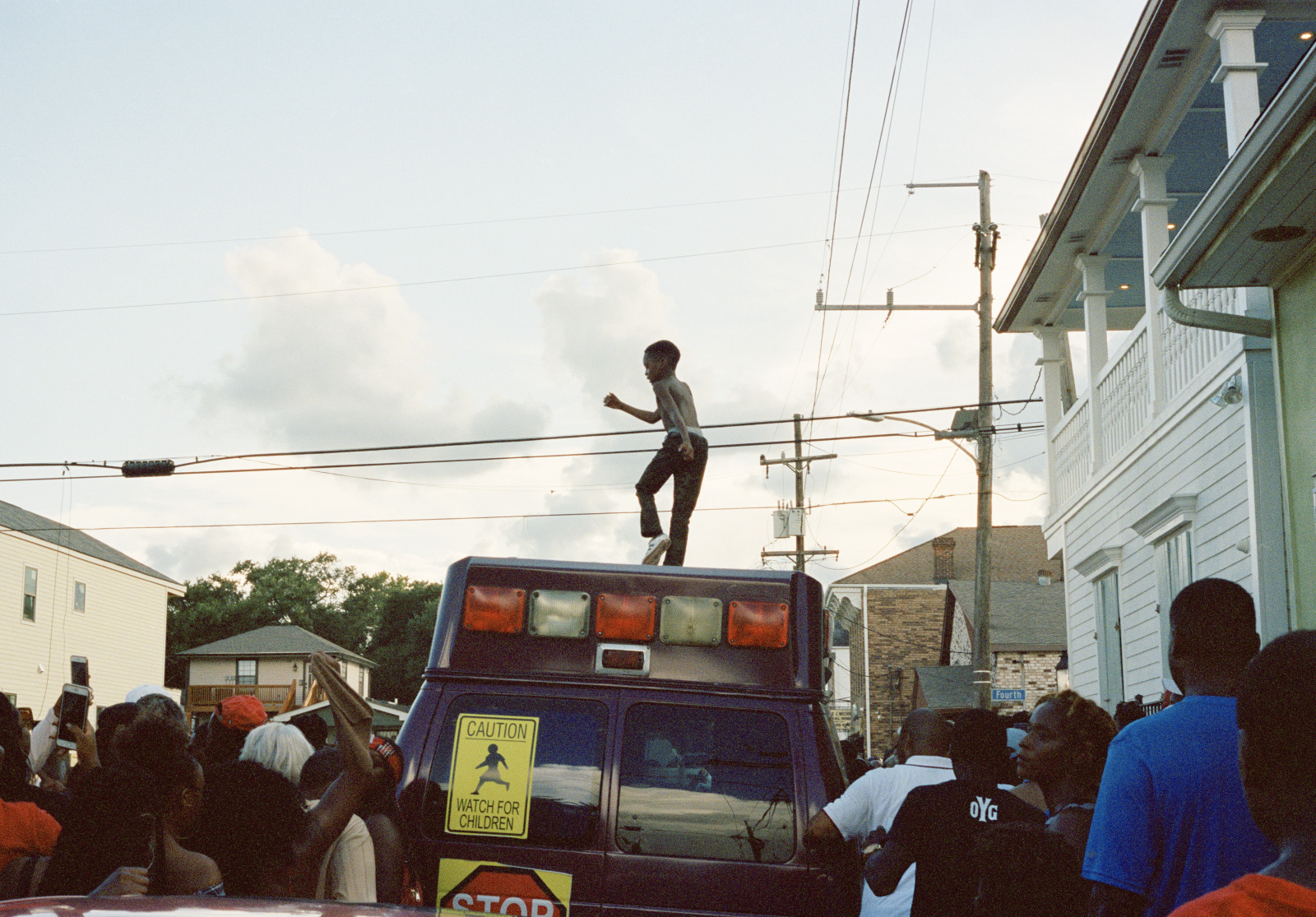 View from the street as a young boy dances on the roof of a pickup truck during a second line parade.