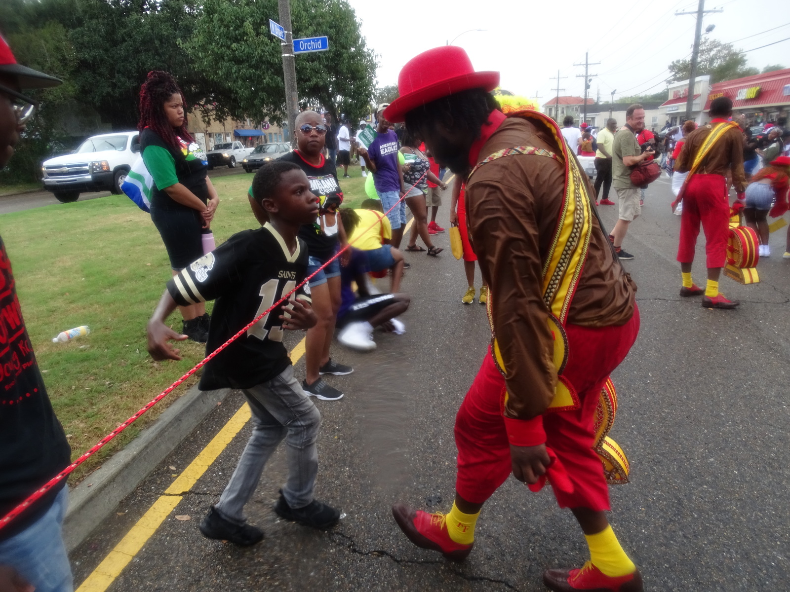 A dancing member of the Footwerk Family, wearing red and gold, looks at a young man wearing a New Orleans Saints jersey at a second line parade.