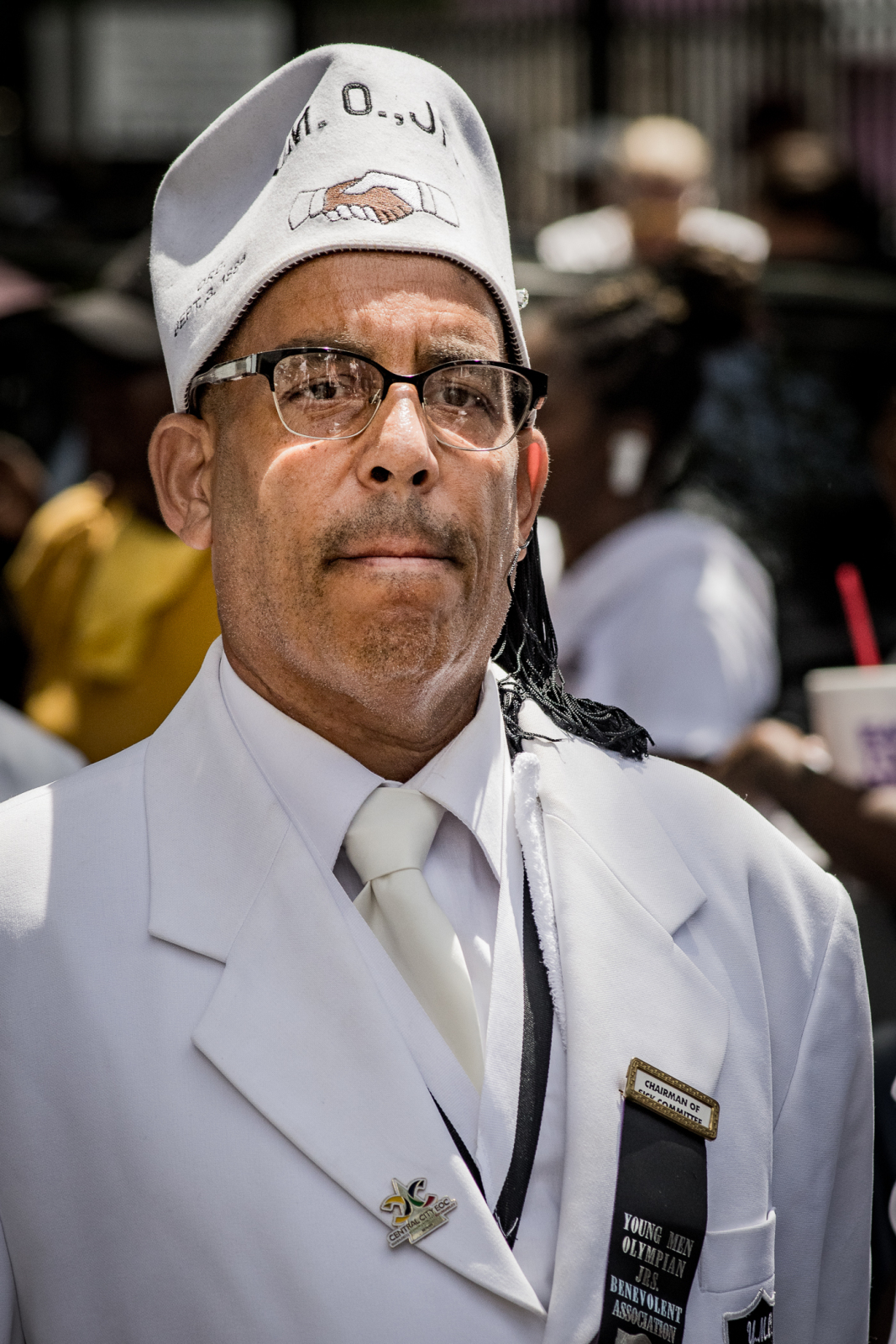 Waldorf “Gip” Gipson III wears a crisp white suite, white tie, and a white hat that has an embroidered picture of two hands (one black and one white) shaking, as a sign of solidarity.
