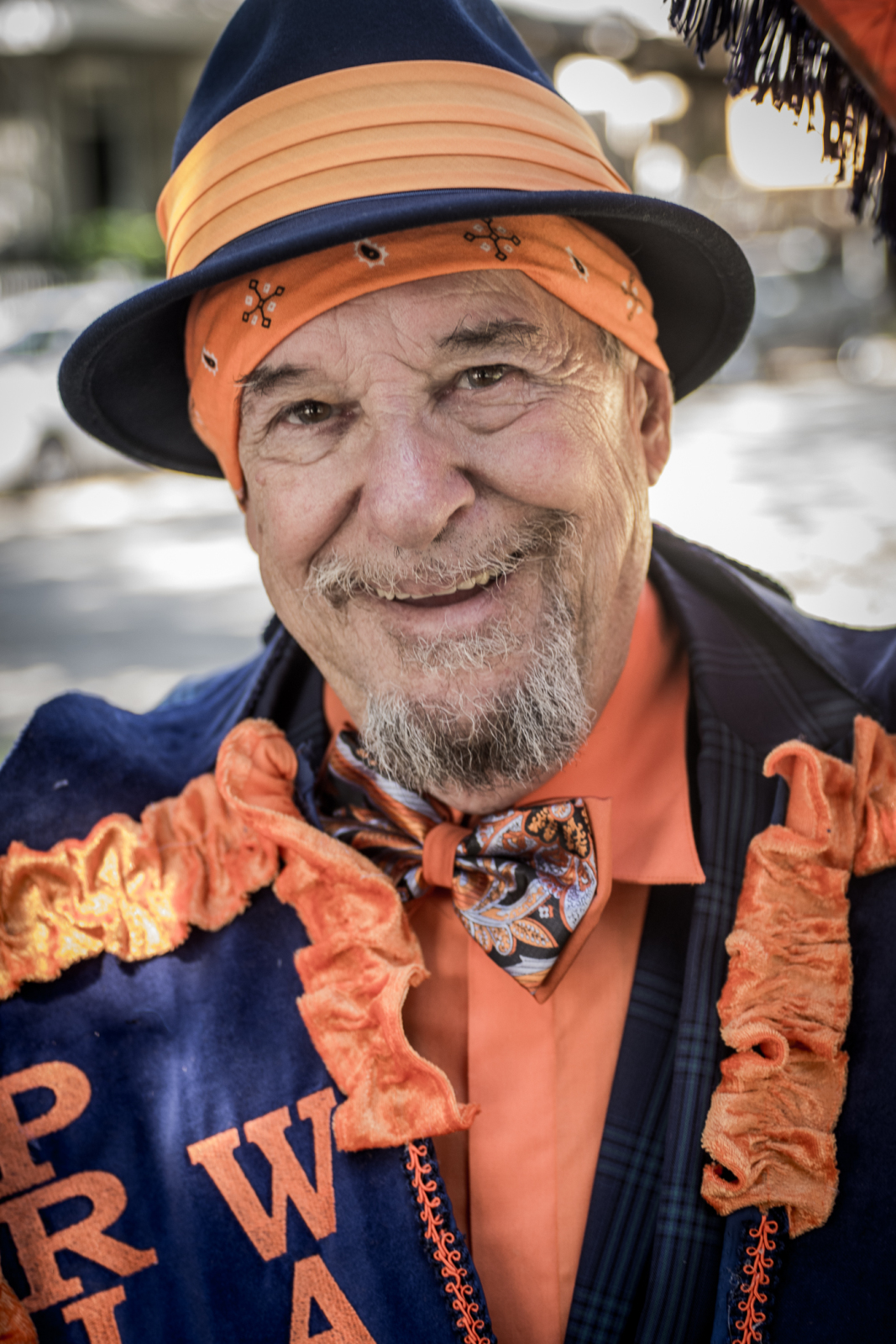 Prince of Wales member Joe Stern smiles at the camera, while wearing a purple hat and coat with orange accents at a second line parade.