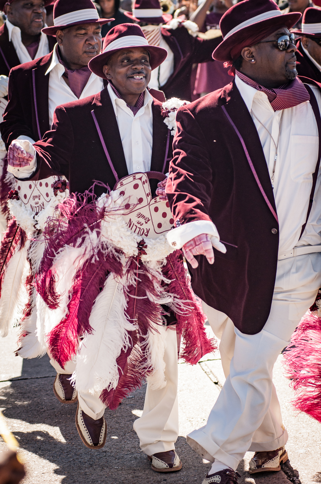 Corey Woods joined by fellow members at a Nine Times parade in 2012. The men are wearing red velvet jackets, white shirts, and matching hats while carrying feathered parade fans.