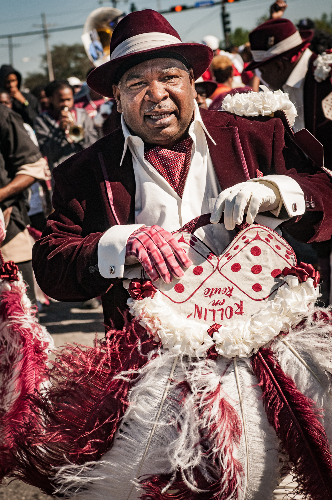 Troy Materre at a Nine Times parade in 2012. He is wearing a velvet maroon jacket and matching hat while carrying a parade fan.