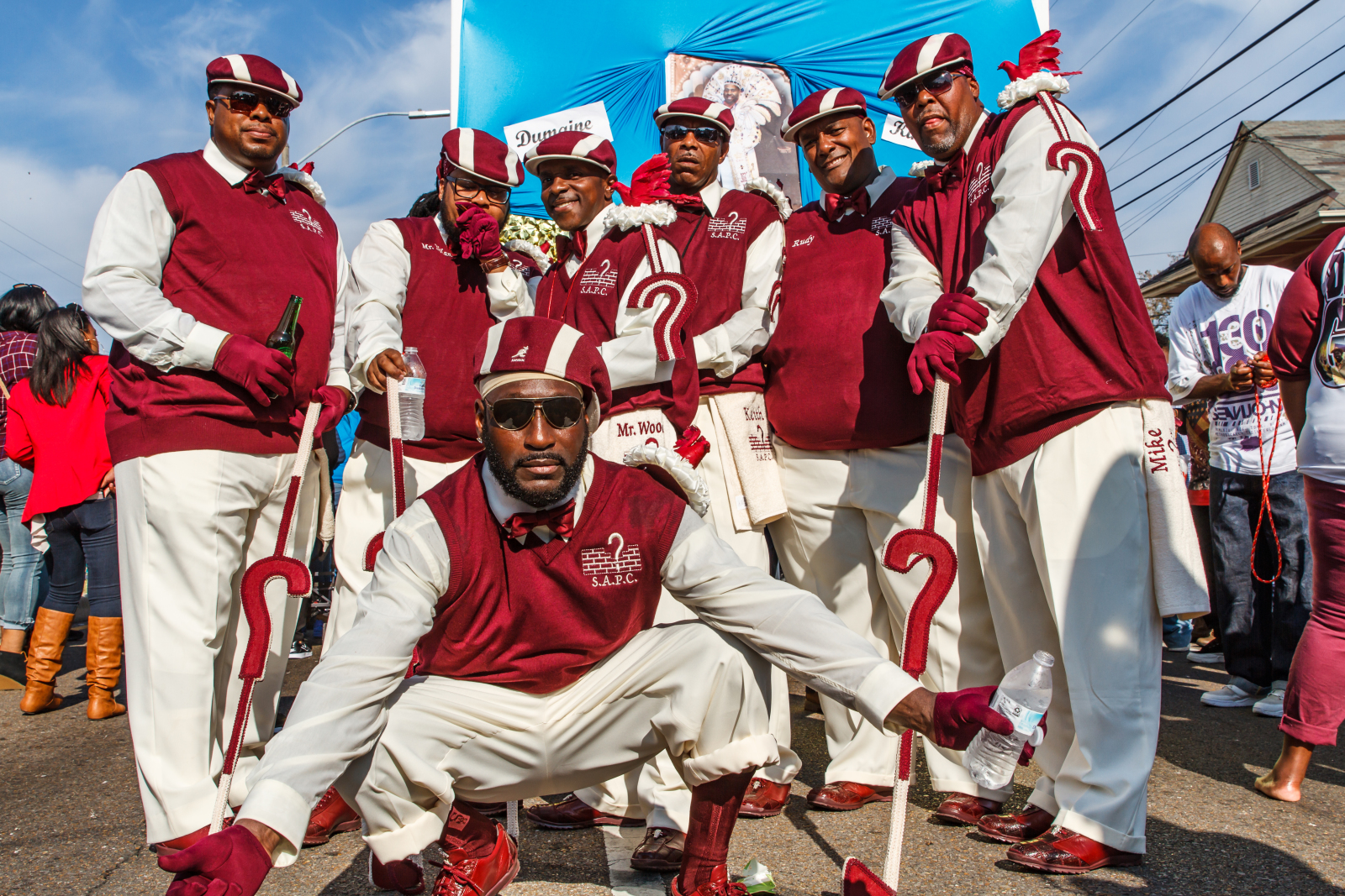 Members of the ? Mark Social and Pleasure Club pose for a photo at the Dumaine Gang parade in 2017. They are wearing red jackets with white long sleeve shirts and white pants.