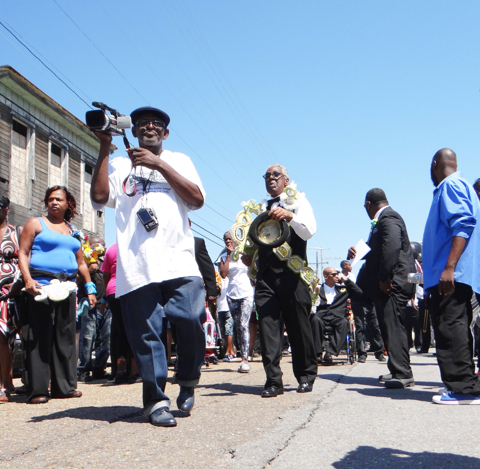 Sylvester Francis, founder of the Backstreet Cultural Museum, films Kennth Dyke’s funeral. Onlookers can be seen on either side of the street.