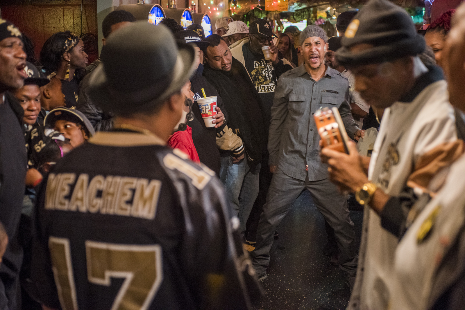 Jeremy Stevenson singing at a Monogram Hunter's practice. He is in a crowded bar setting, surrounded by fellow members of the community,
