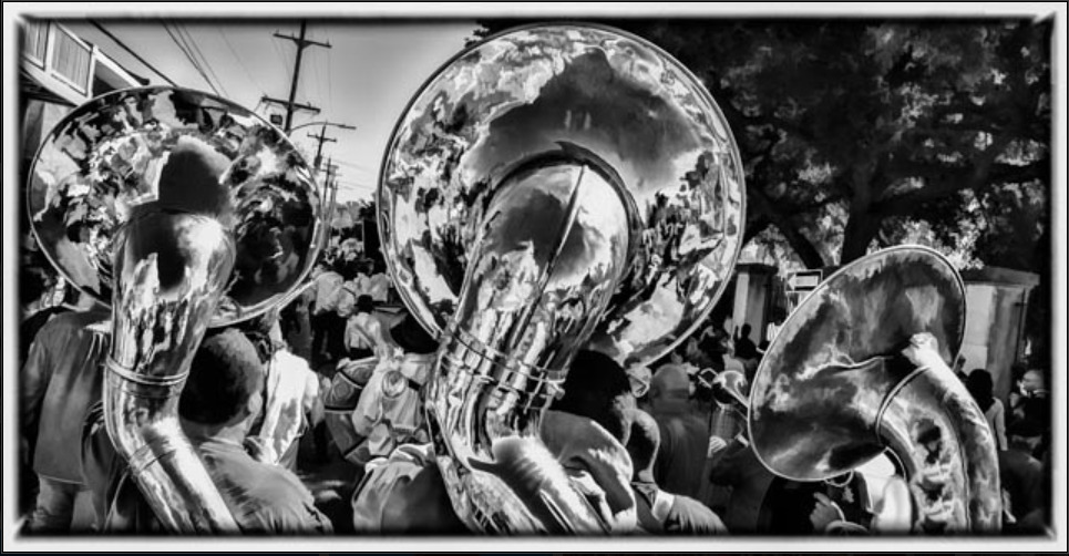Black and white photo of a Sudan parade, which is focused on the reflection of a crowd in the sousaphone bells of a brass band.