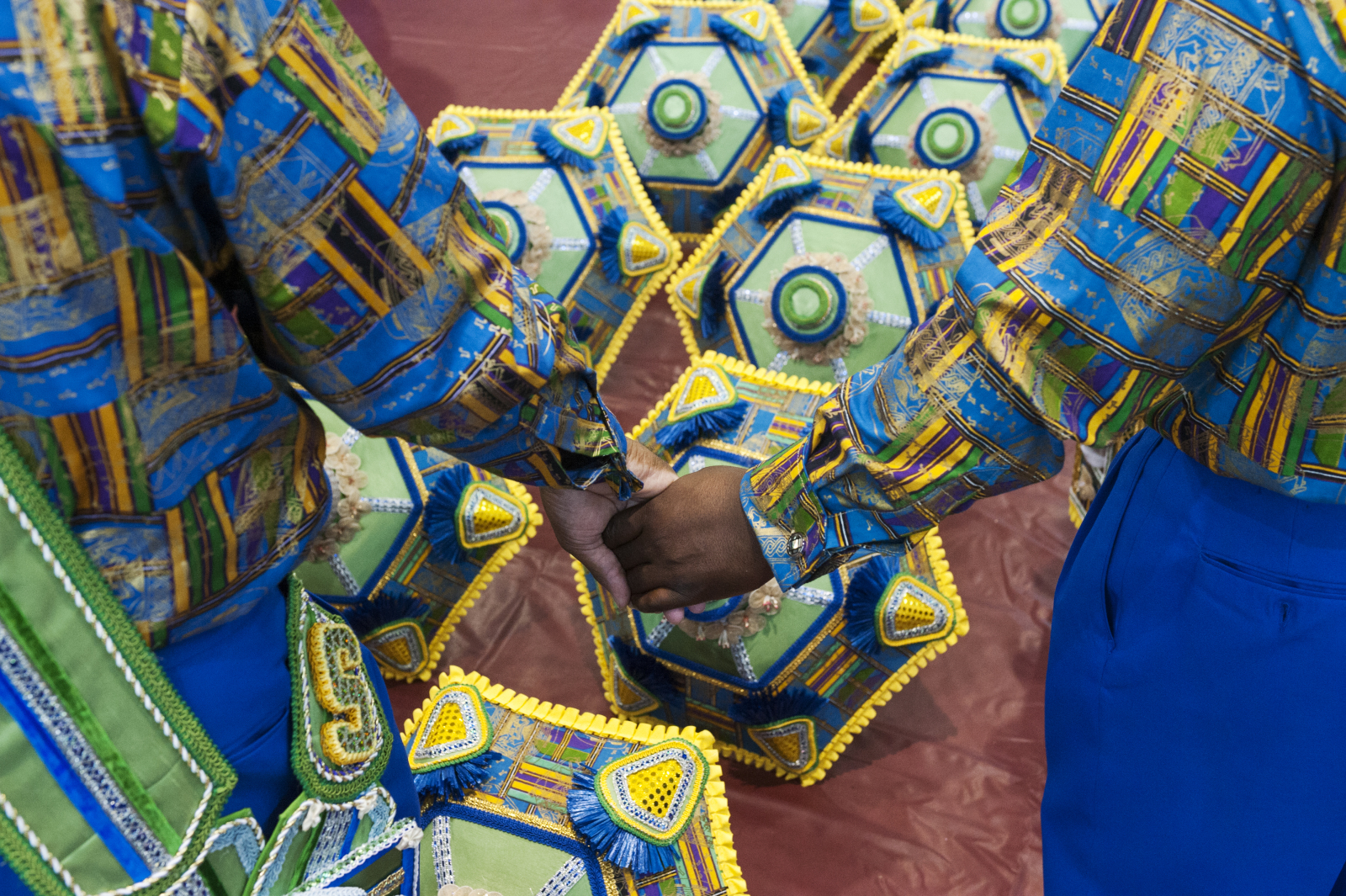 Two members of the Sudan social aid and pleasure club hold hands before beginning a parade. They are wearing bright patterned shirts, with a view of decorated parasols lined up on the ground in the background.