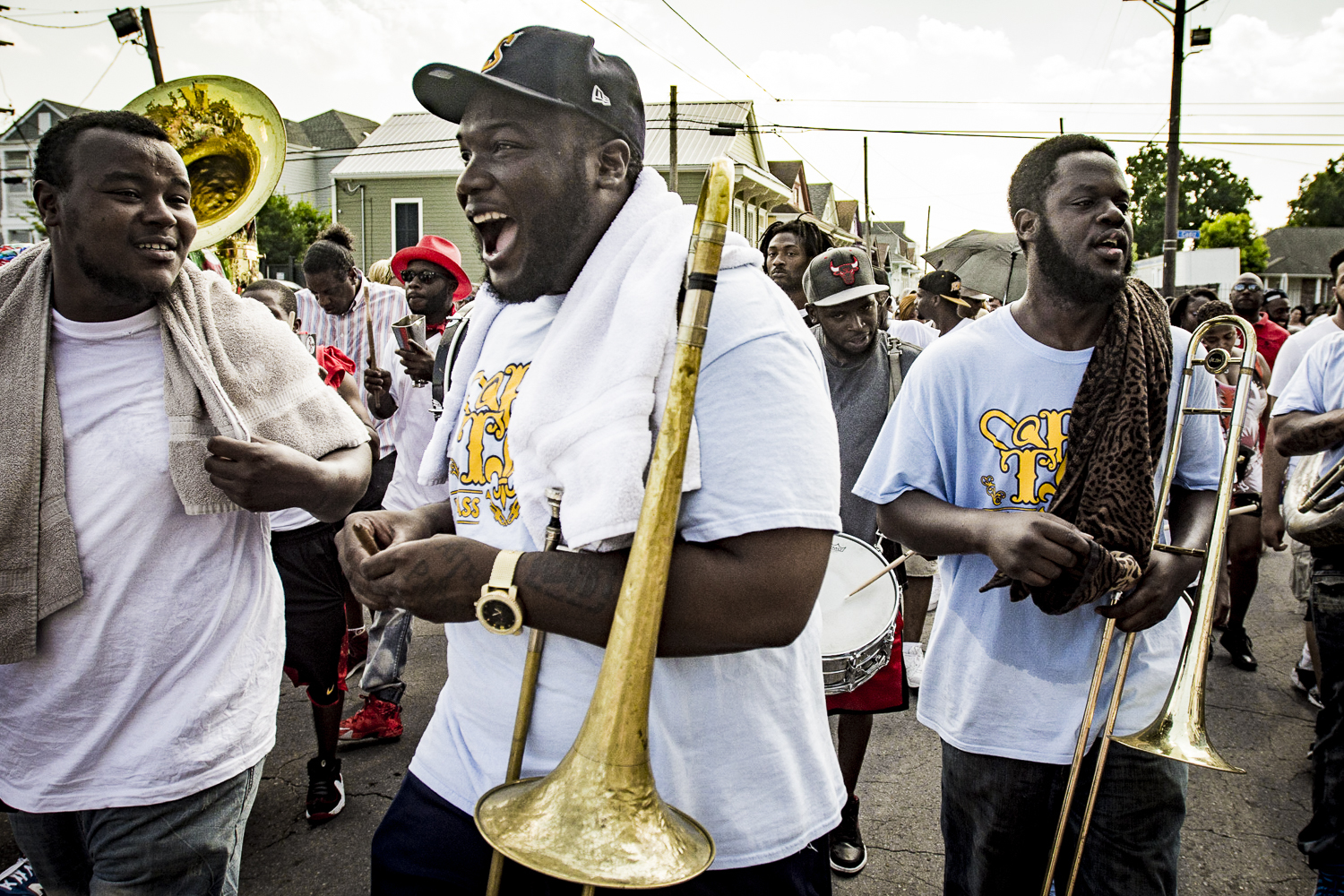 A lively second line parade features musicians laughing, playing instruments, and engaging with the crowd.