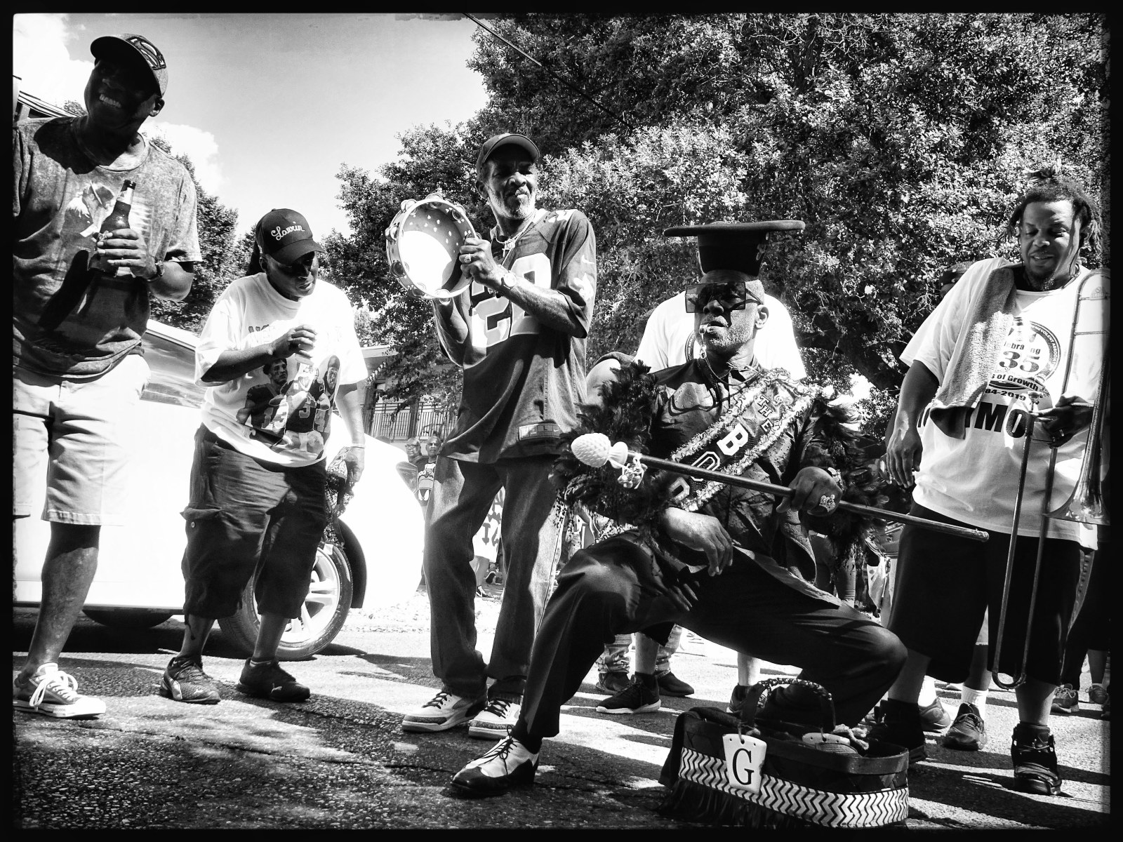 A black and white photo shows Gregg Stafford, YMO Jr. dancing with a baton in front of a brass band at the 135th anniversary parade in 2019.