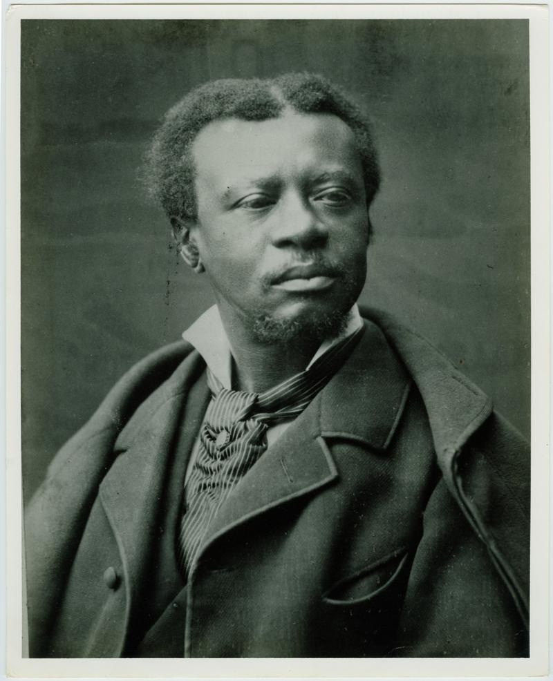 A black and white portrait of a Edmund Dede with short, curly hair and a pointed beard. He is wearing a suit with a tie and looking slightly to his left. The expression is serious, with a thoughtful gaze. The background is plain.